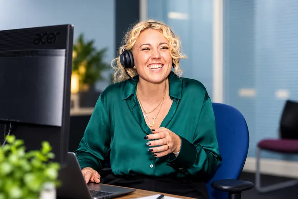 A team member in a green top speaking on a headset in the office